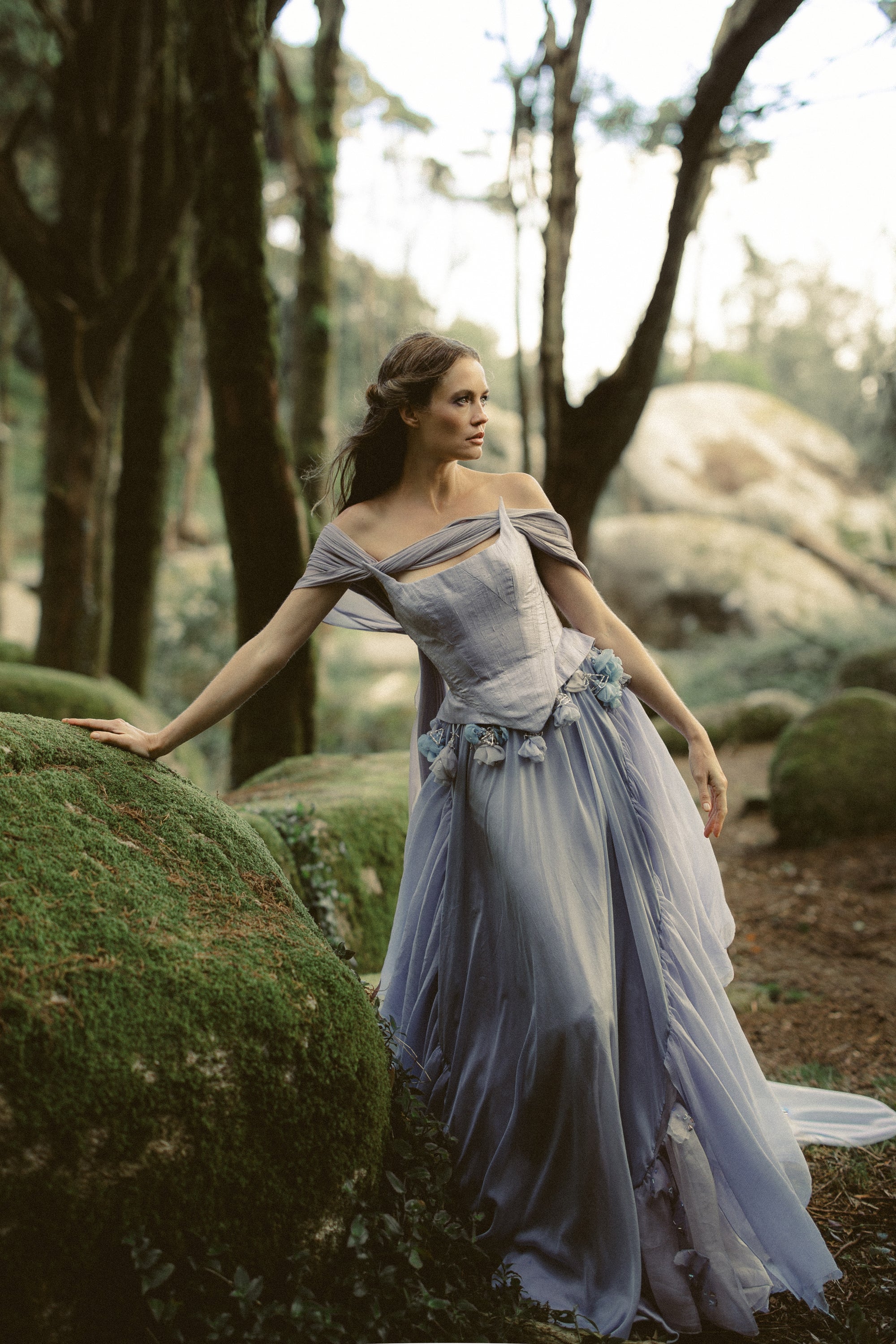 Blooming Belt styled with a whimsical blue bridal gown, full-length view on mossy rocks in enchanted forest by MYWONY