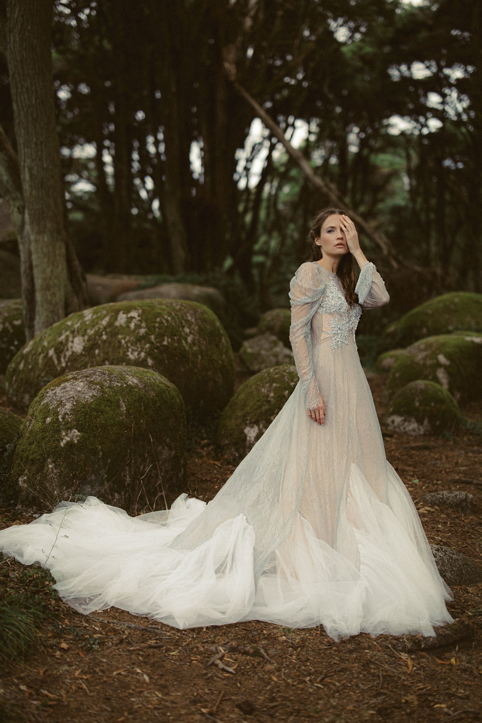 Elystra whimsical wedding dress full-length — dove-grey lace gown with long train and draped sleeves on mossy forest floor by MYWONY