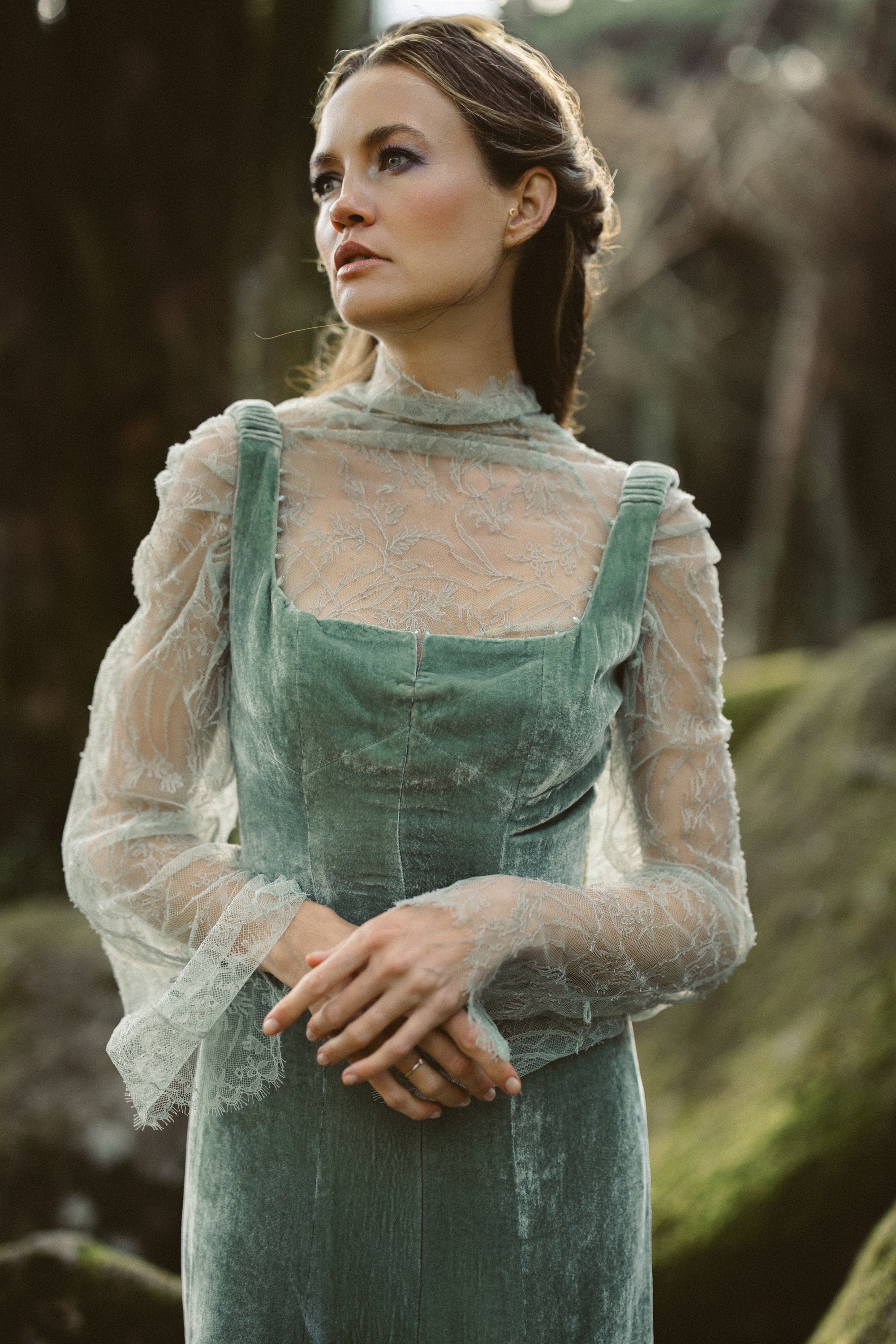 Miryelle boho wedding dress by MYWONY — close-up portrait showing the sheer high-neck lace top layered over a pale moss-green silk velour gown with square neckline, styled in a whimsical forest setting