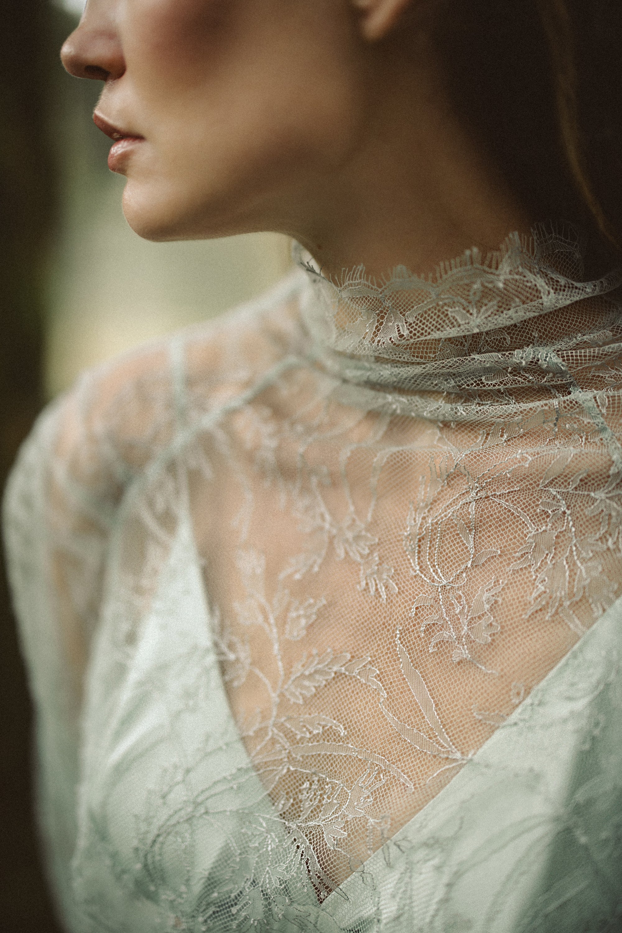 A macro detail shot highlights the exquisite craftsmanship of the Miryelle lace top, focusing on the sheer high neckline with delicate eyelash lace edging. The image captures the intricate floral motifs of the pale moss-green lace layered over a matching silk triangle bra, emphasizing the ensemble's ethereal and romantic texture.