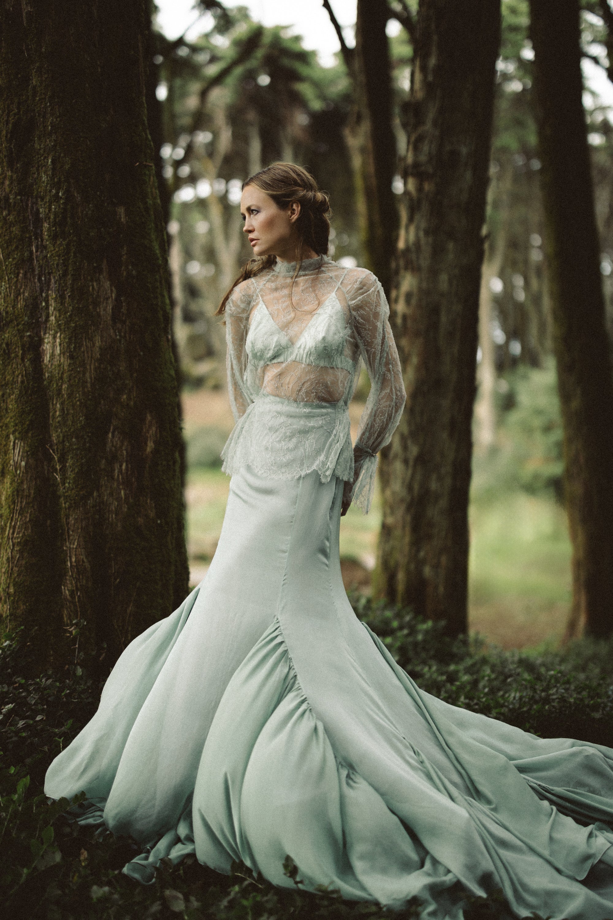 Model wearing complete Miryelle whimsical wedding outfit — silk chiffon skirt with mermaid silhouette and lace top in sage green, standing in an enchanted forest by MYWONY