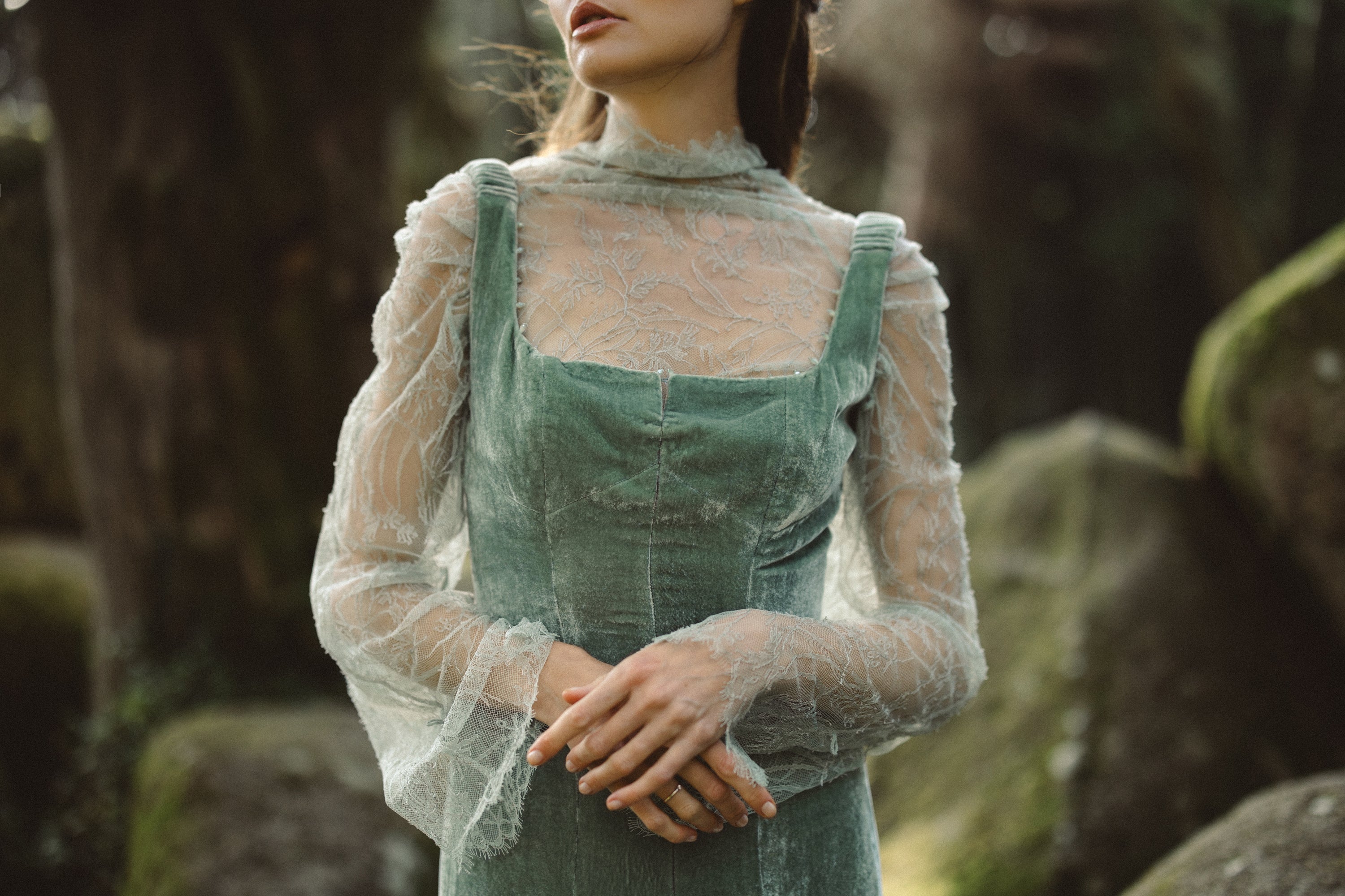 A romantic detail shot captures the Miryelle ensemble, featuring a pale moss-green silk velour bodice with a structured square neckline and gathered shoulder straps. Layered underneath, a sheer high-neck lace top with intricate floral patterns adds a delicate, ethereal texture to the vintage-inspired silhouette.